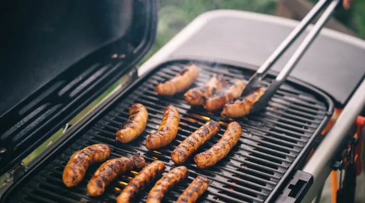 Close-up view of someone using tongs to rotate sausages on a barbeque.