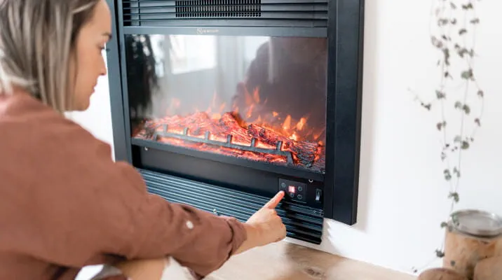 An adult presses a button to operate a modern wood burning fireplace.