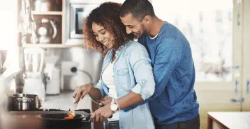 Man holding partner as she prepares a meal on the stove