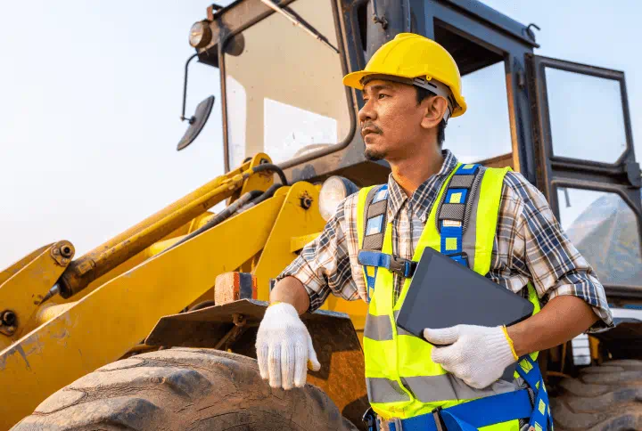 A contractor in safety gear standing beside a large tractor