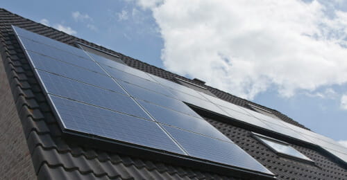 Solar panel installation on the roof of a house reflecting clouds in the sky.