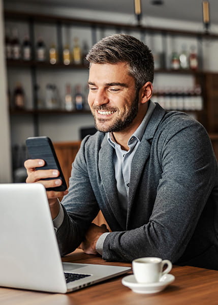 A happy businessman is sitting in a coffee shop and checking on his bank account on the mobile.