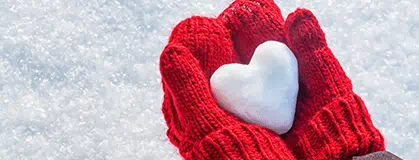 Hands in knitted mittens with heart of snow in winter day. 