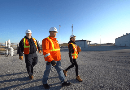 Three people wearing safety vests and helmets walking