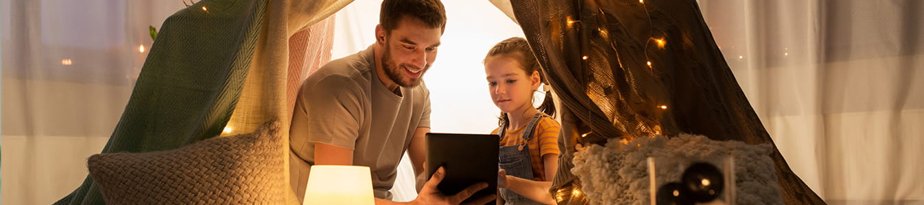 Happy father and little daughter with tablet pc computer in kids tent at night at home.