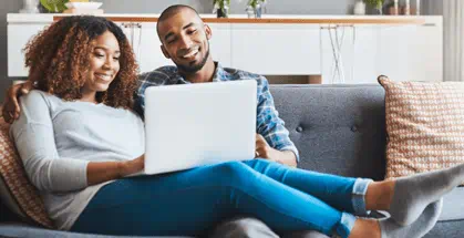 Young couple relaxing on the sofa at home and using a laptop together.