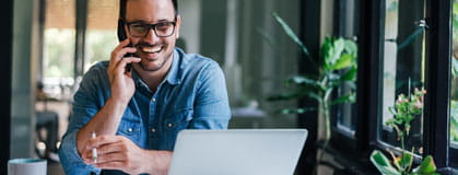 Portrait of young smiling cheerful entrepreneur in casual office making phone call while working with laptop