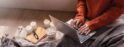 Top view of woman in sweater hands typing computer with cup of hot chocolate winter time at home.