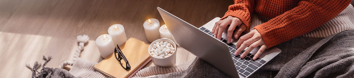 Top view of woman in sweater hands typing computer with cup of hot chocolate winter time at home.