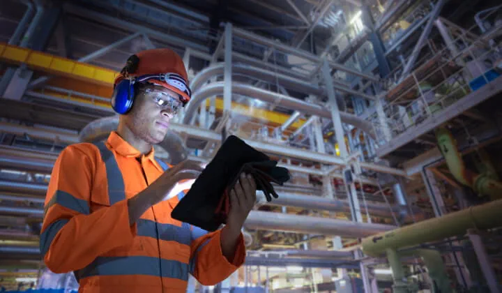 A technician using a tablet while standing in a large mechanical room.