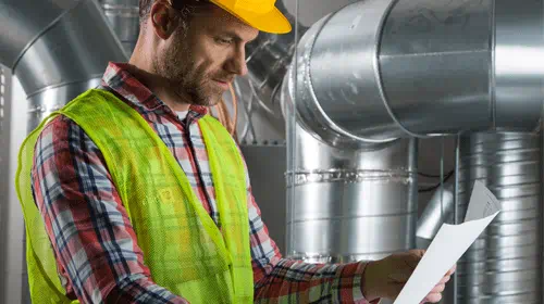 A man in a hard hat examining a blueprint in a factory.