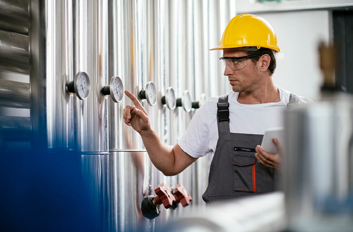 Man at work wearing a yellow hard hat and safety goggles while holding a tablet.