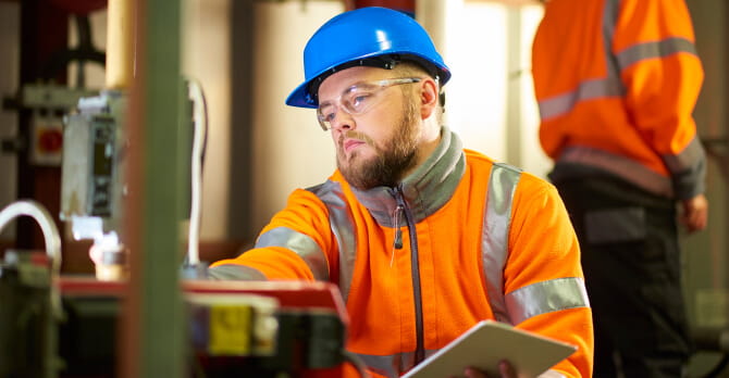 Man in hard hat kneeling to inspect boiler room machinery