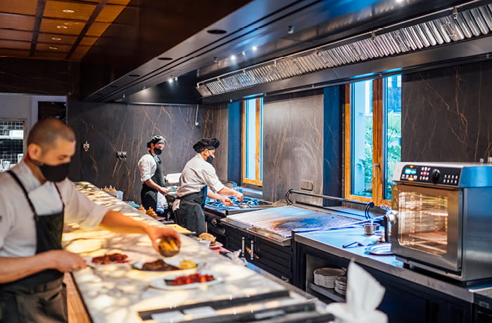 Three people working in a commercial kitchen with protective face masks on.