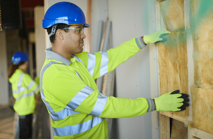 Man in hard hat and protective goggles installing wall insulation.