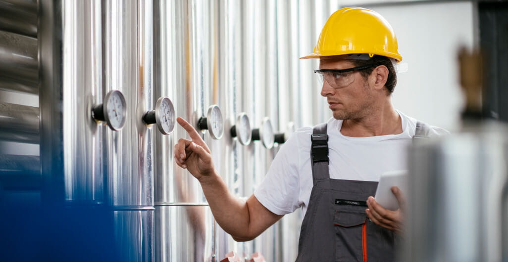 Man at work wearing a yellow hard hat and safety goggles while holding a tablet