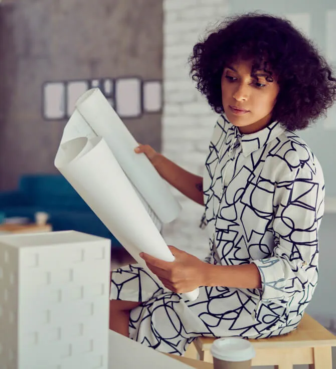 Woman sitting in office holding blueprint and examining 3D model