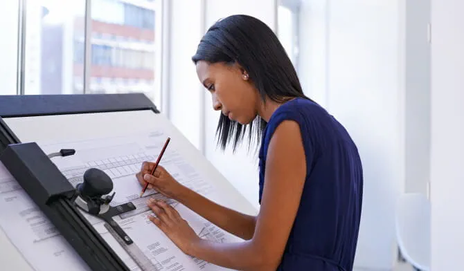 Woman standing at drawing board looking at blueprints