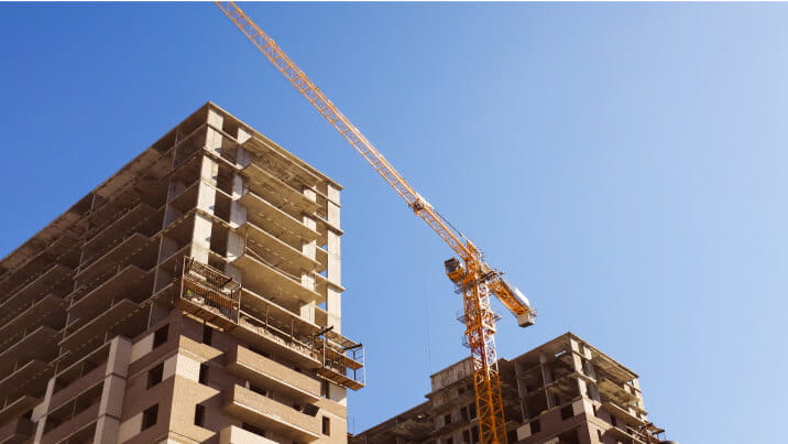 Two large condominium towers under construction on a clear day. A crane operates between the two buildings. 