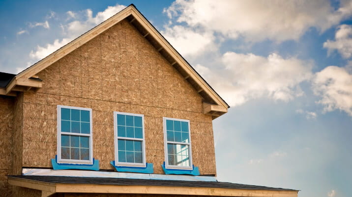 Exterior view of a home’s construction frame with newly applied windows on a sunny day.