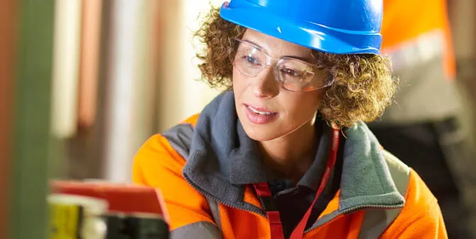 Woman with hard hat and goggles inspecting a boiler room pump