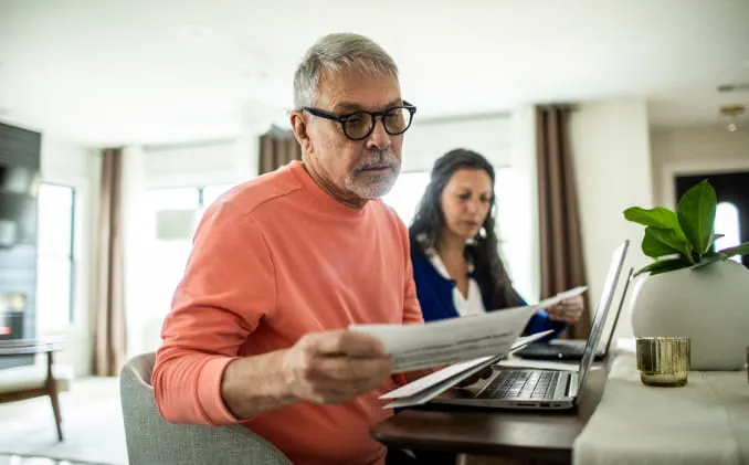 Two people sit in front of laptops, looking at their bills. 