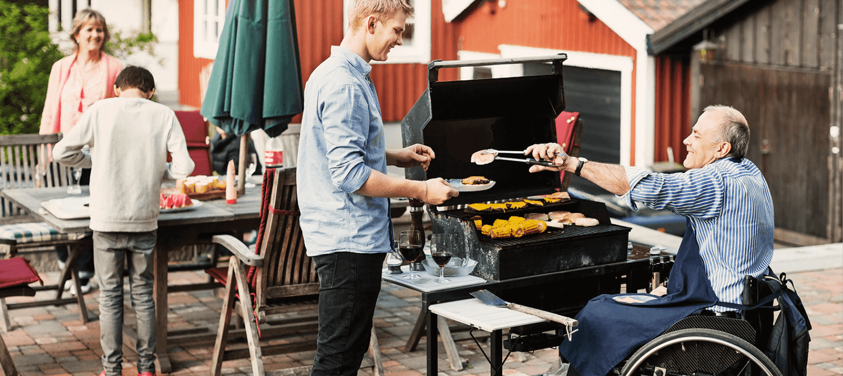 Man in wheelchair grilling and serving food to his son while the rest of family sets the table