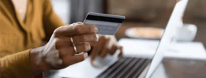 Hand holding a credit card by a laptop.