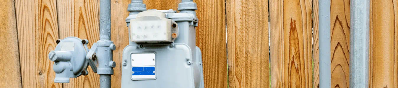 Natural gas meter in residential suburban backyard with wooden fence in background.