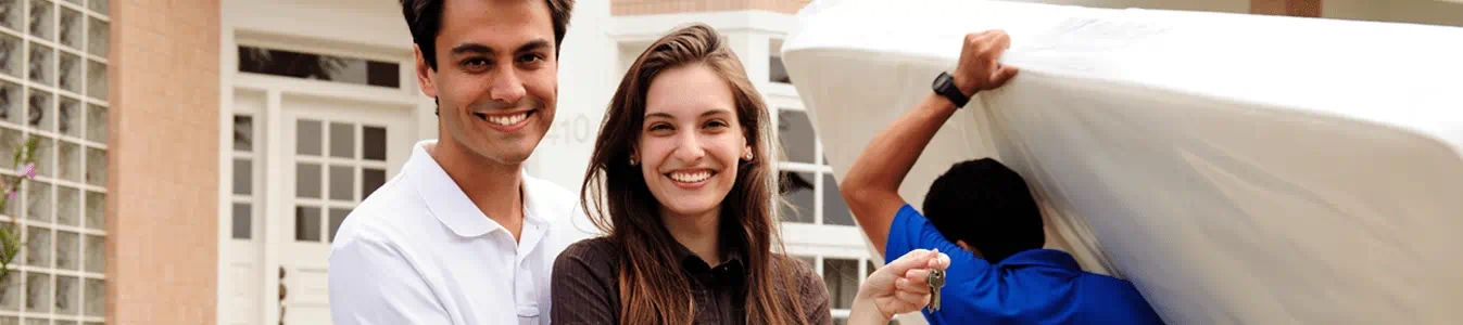 A couple smiling and a person moving a mattress