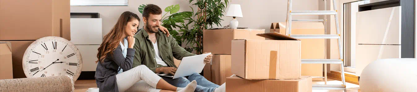 A couple sitting on the floor with several boxes for moving