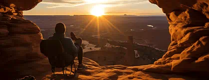 A person sitting on a cliff looking at the sunset